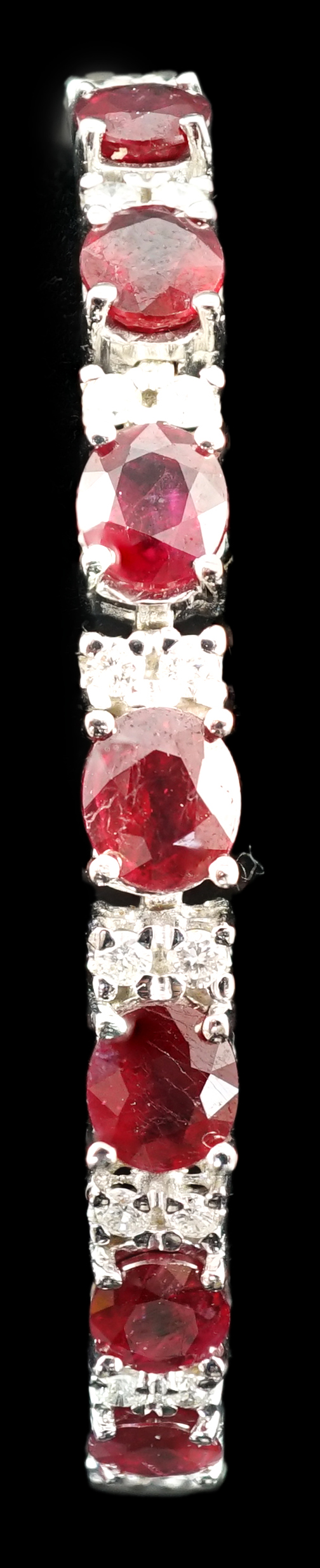 A 750 white gold and seven stone oval cut ruby set line bracelet, set with sixteen stone diamond spacers